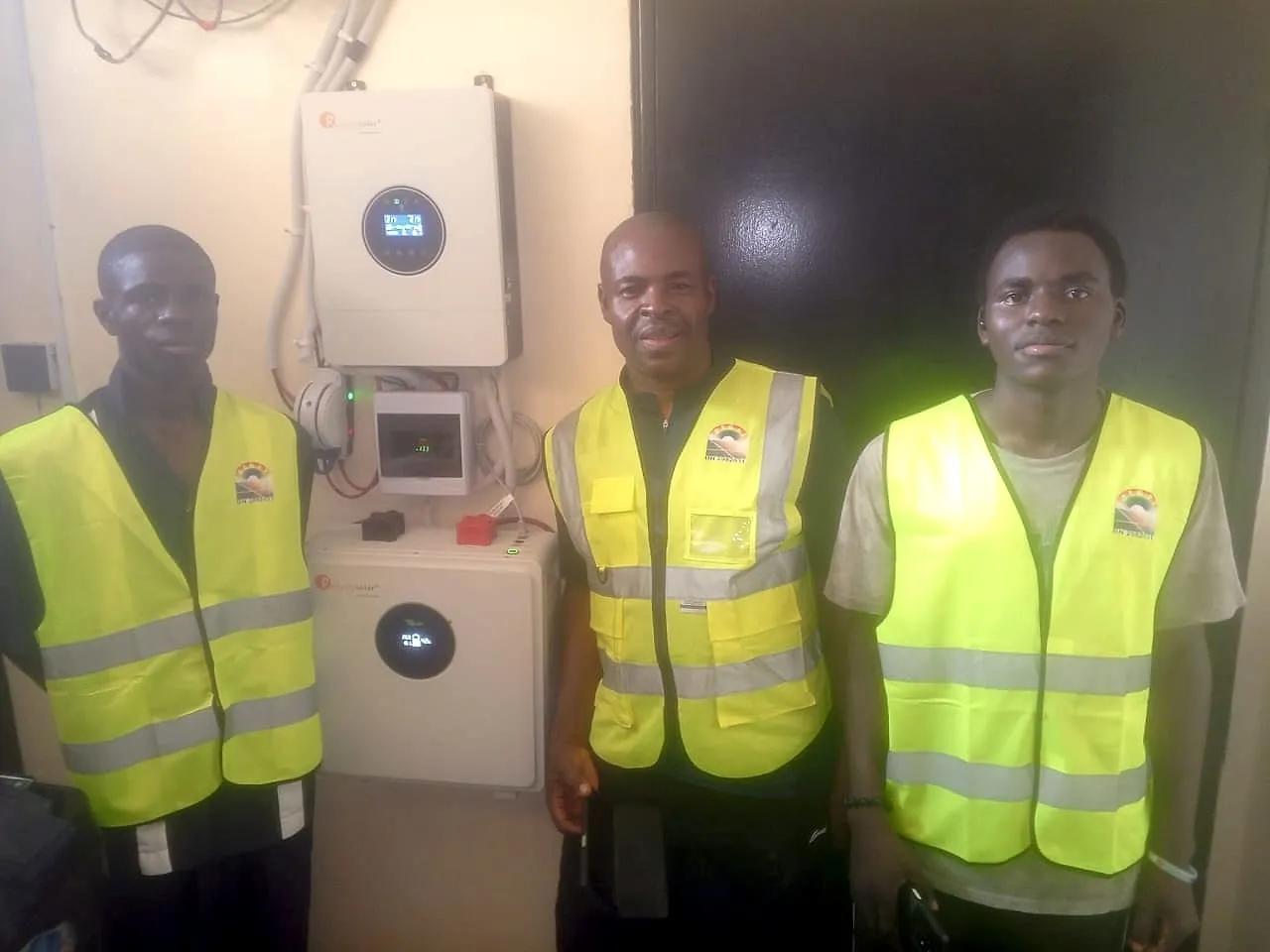 Three Eskor installers in hi-vis vests standing beside a newly commissioned hybrid inverter and lithium battery