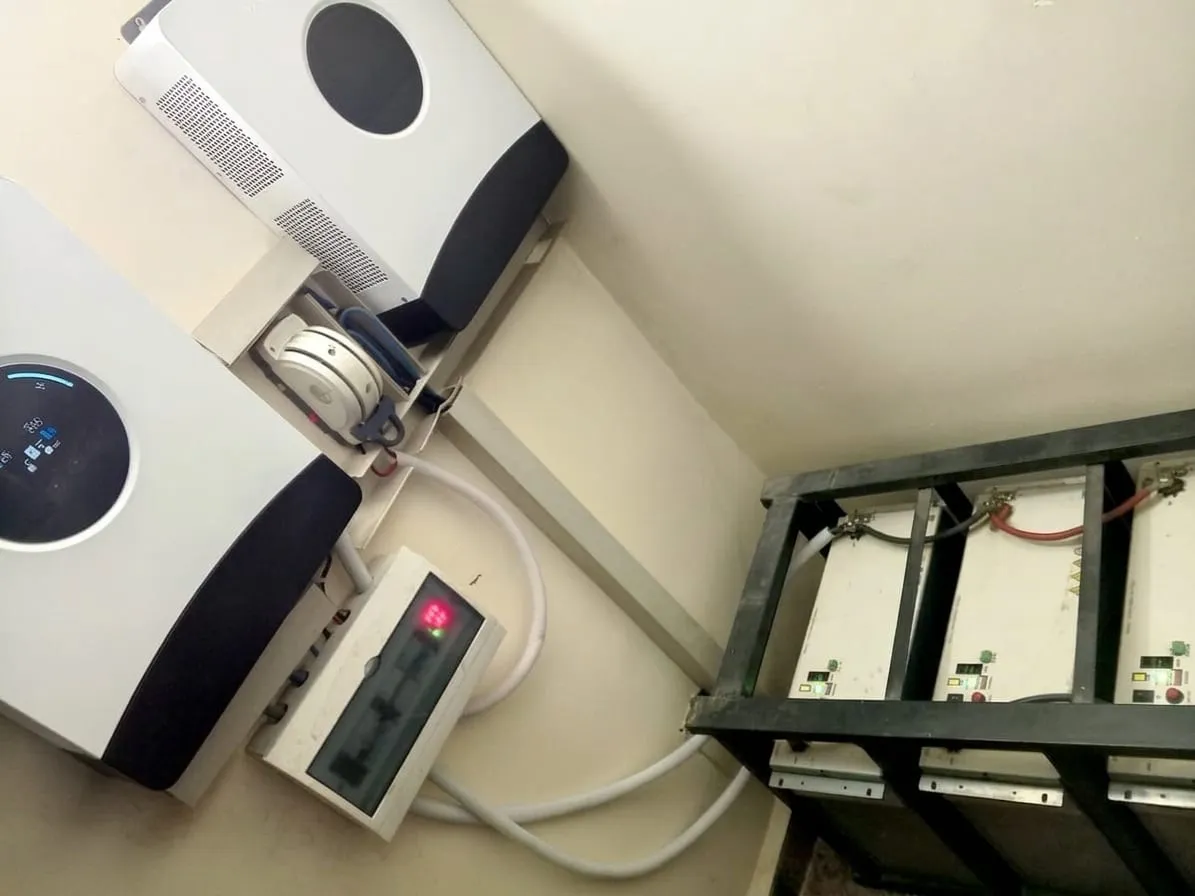 Two hybrid inverters mounted on a wall above a rack of lithium batteries